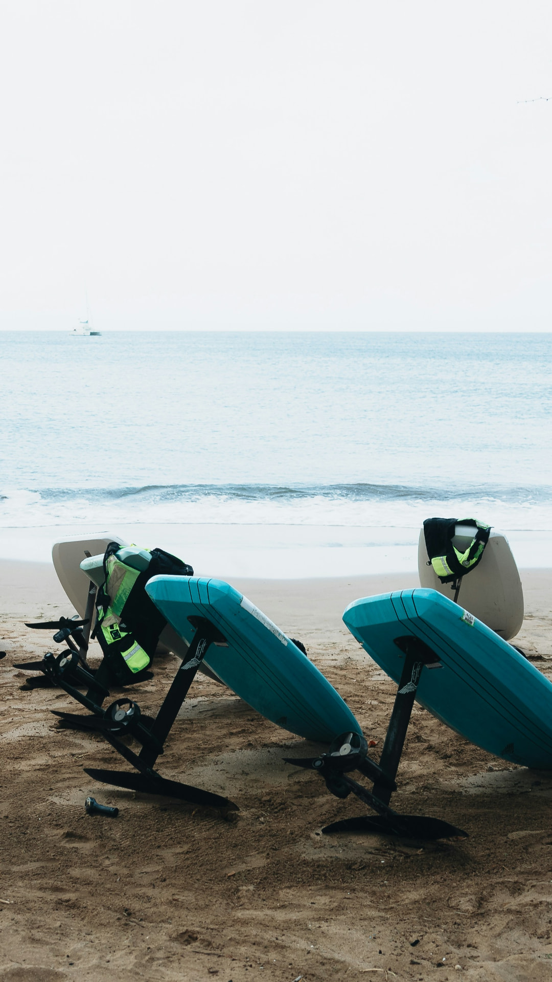 A fleet of e-foil boards resting on the sand above the tide line