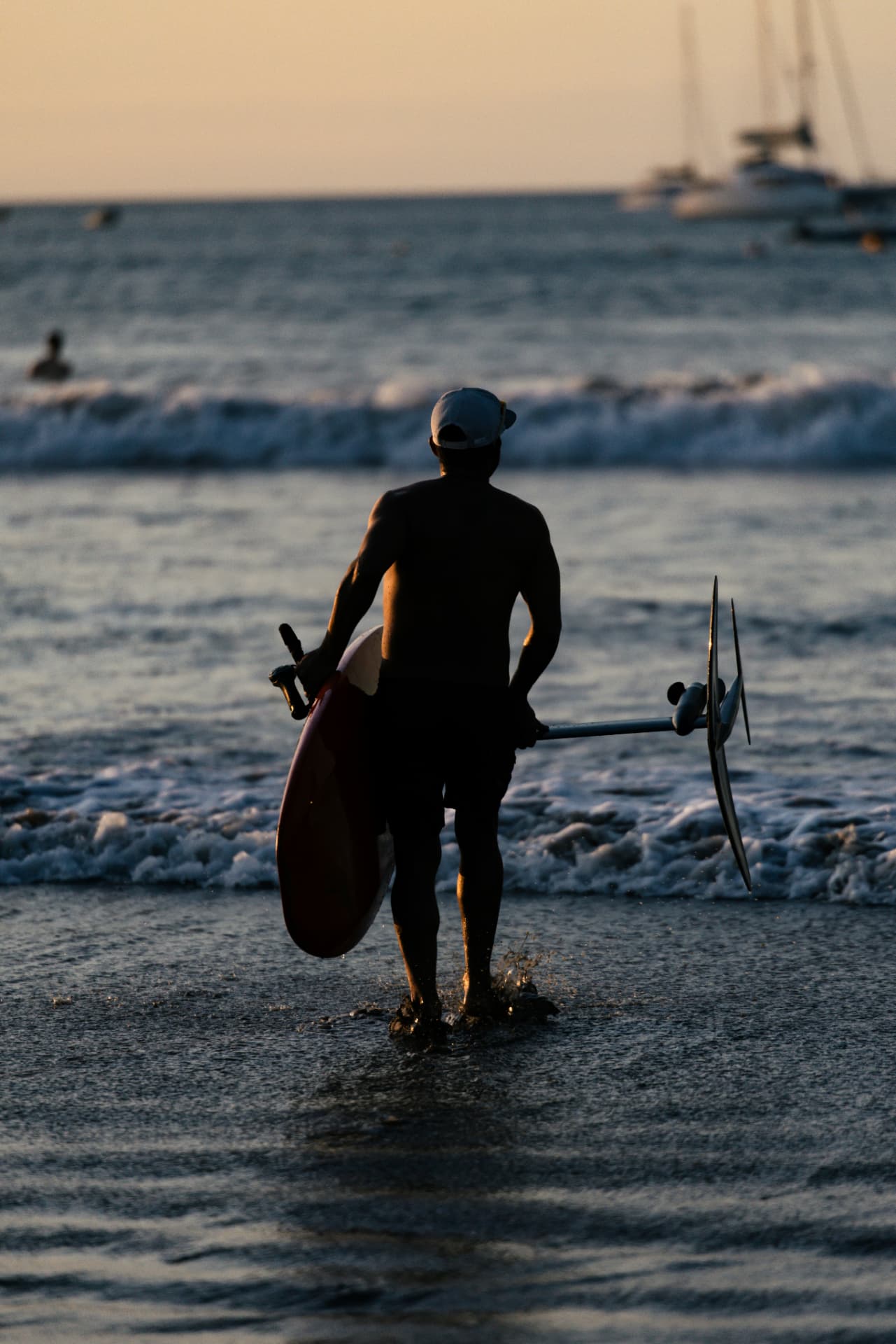 A rider carrying a foil board through the shallows at sunset